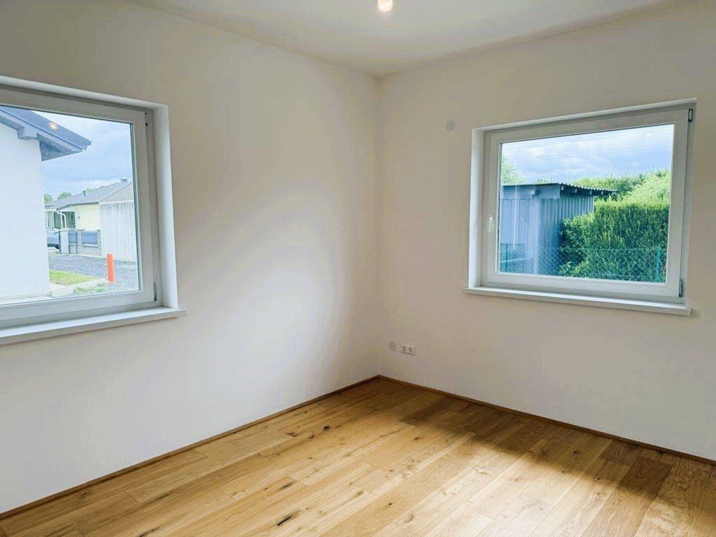 Helles Zimmer mit Holzparkettboden und zwei Fenstern.