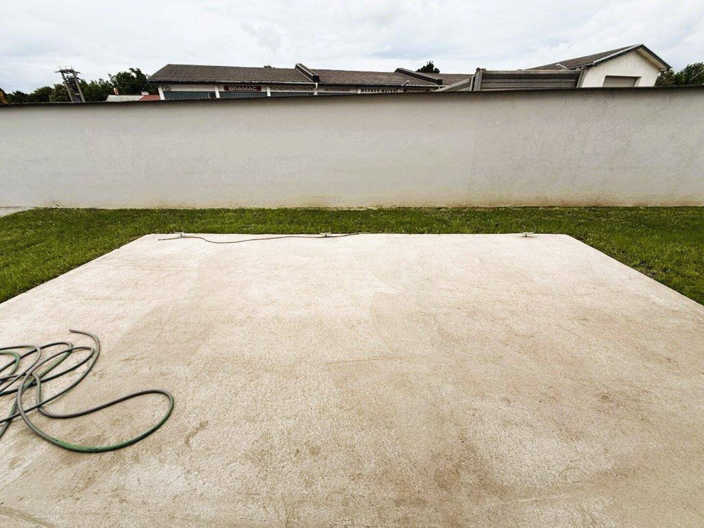 Gartenbereich mit Rasenfläche und einer vorbereiteten Betonplatte.