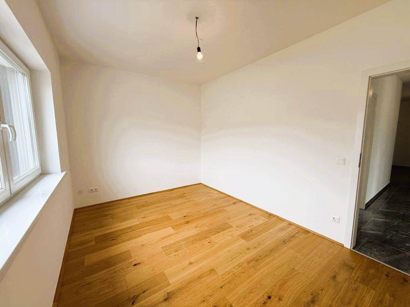 Leeres Zimmer mit Holzparkettboden und Zugang zu einem gefliesten Bereich.