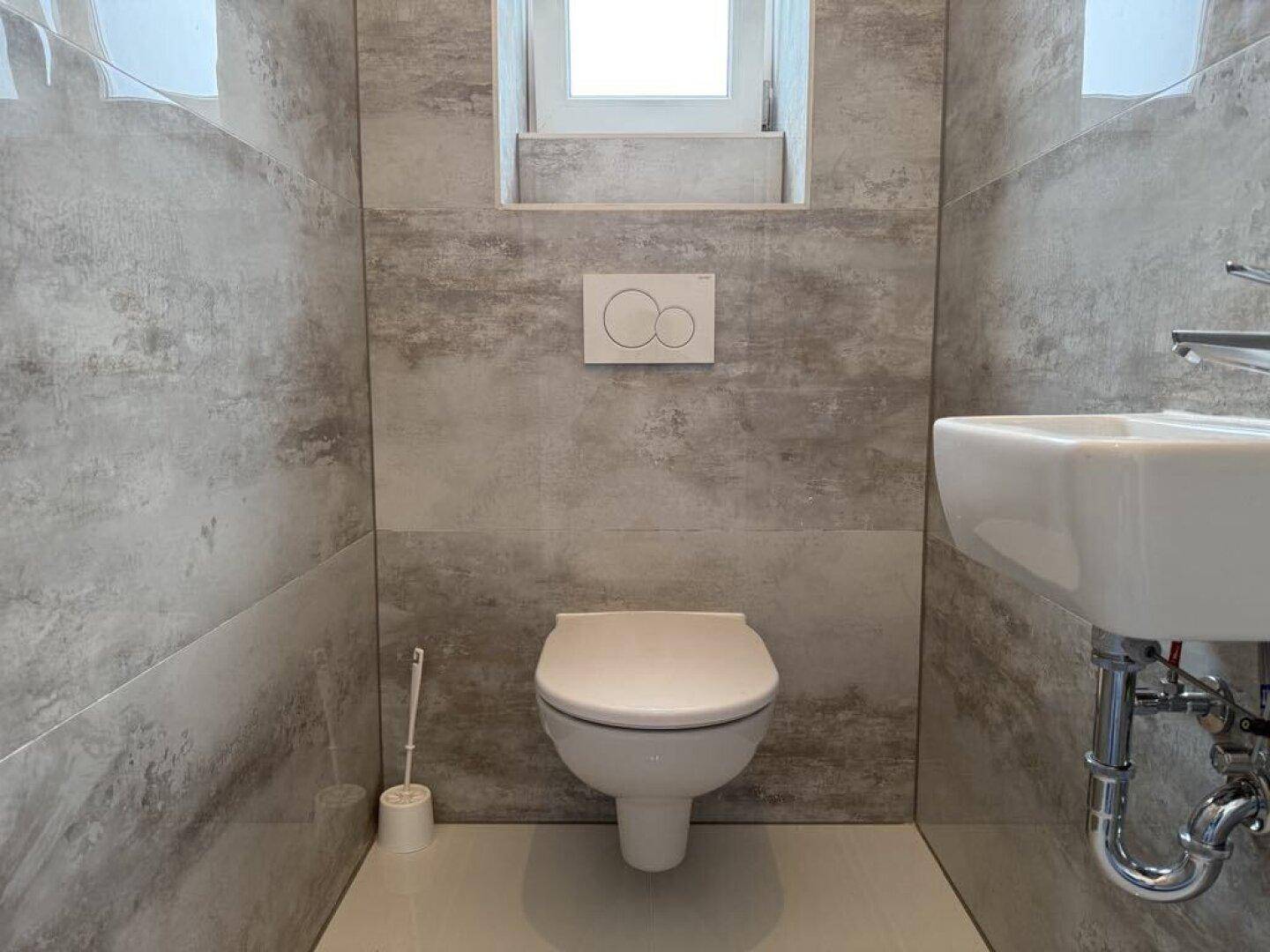 Gäste-WC mit wandhängender Toilette, kleinem Waschbecken und Fenster.