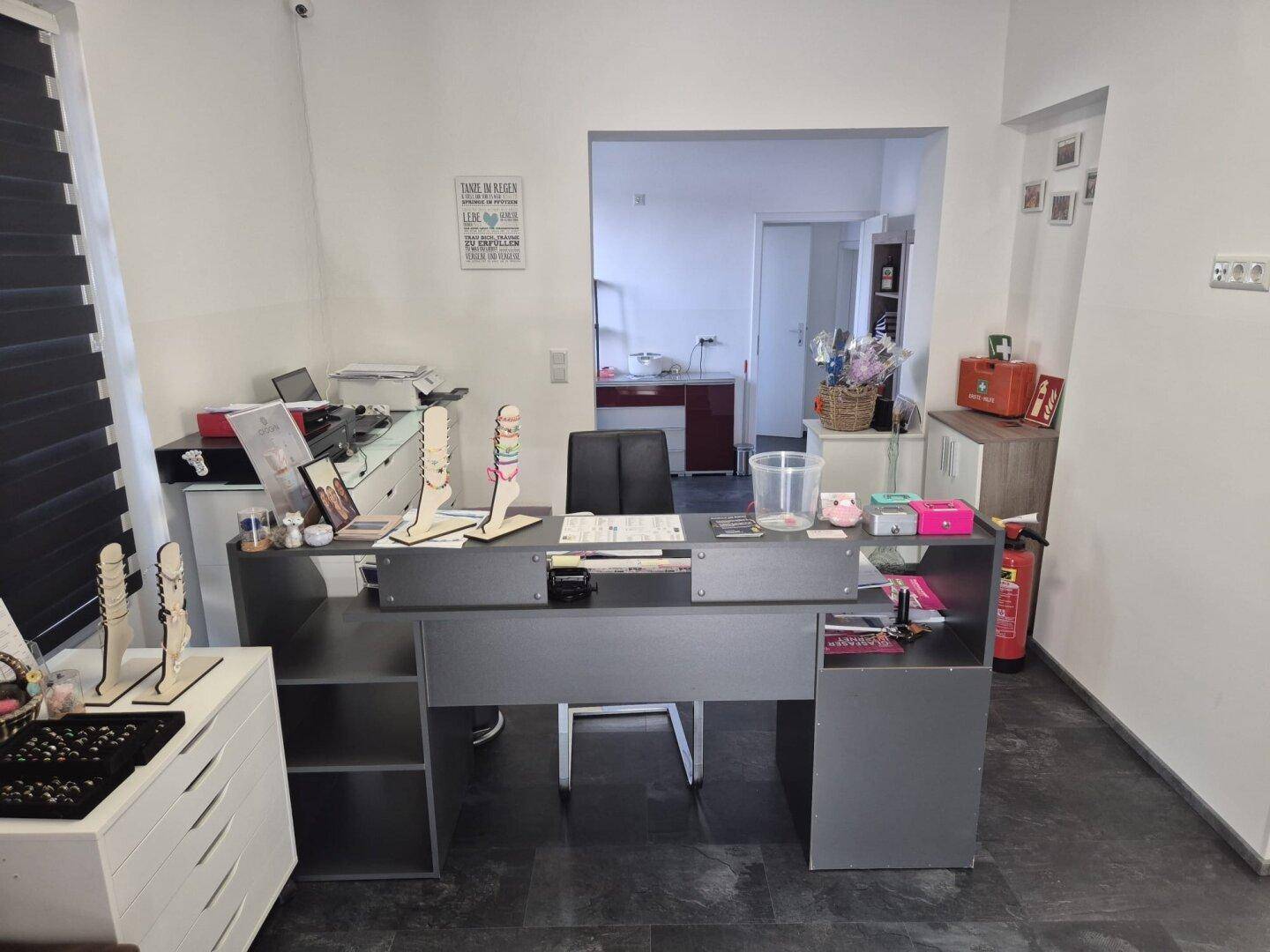 Empfangsbereich oder Büro mit Schreibtisch, dunklem Fliesenboden und Durchgang zu einem weiteren Raum.