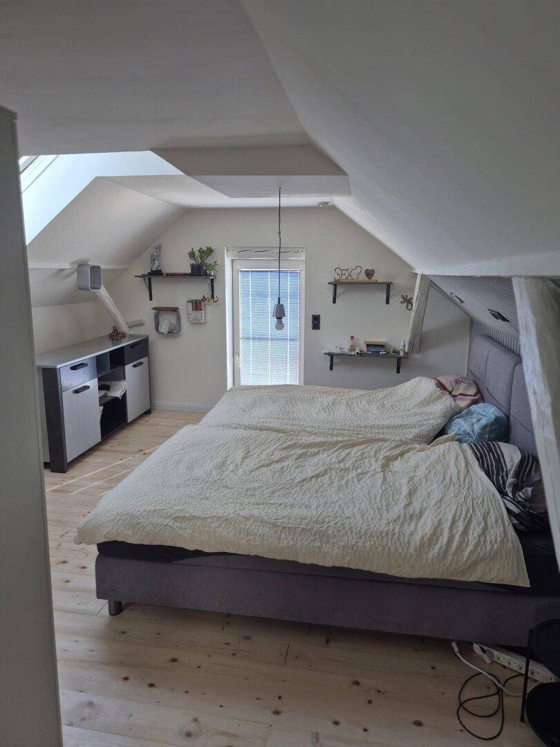 Schlafzimmer im Dachgeschoss mit Doppelbett, Holzboden, Dachfenster und schrägen Wänden.