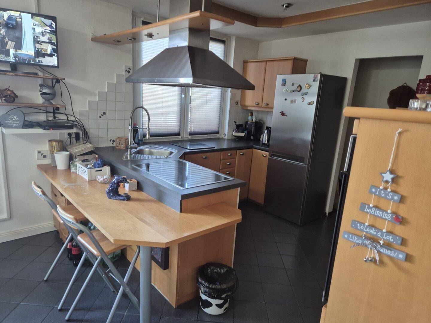 Geräumige Küche mit Kochinsel, modernen Edelstahlgeräten und dunklem Fliesenboden.