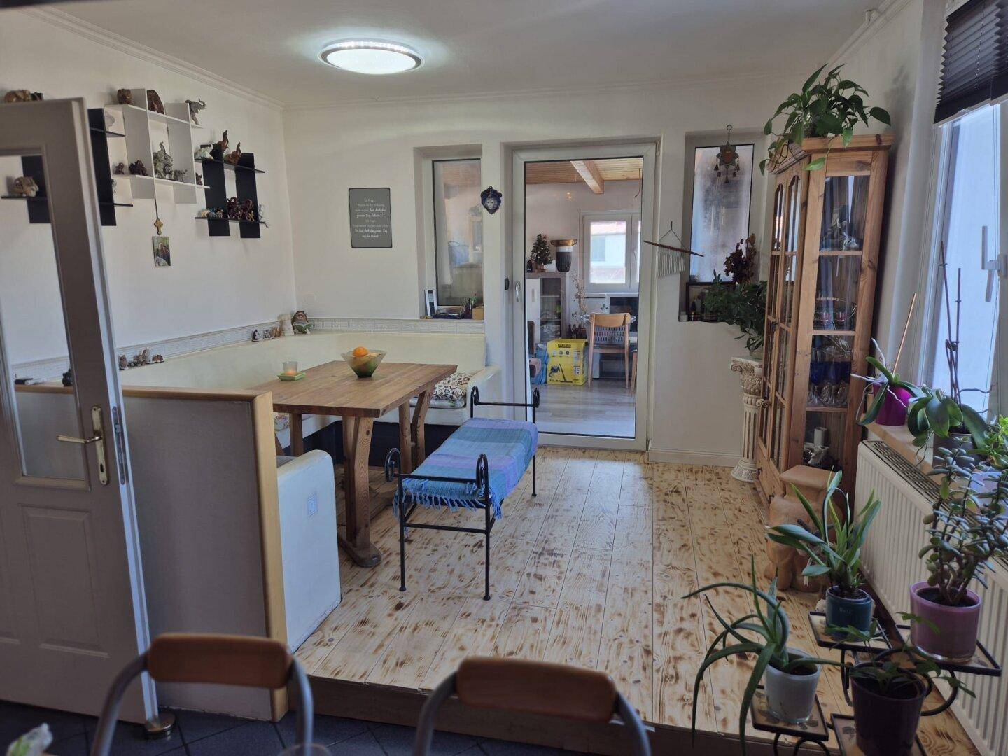 Heller Essbereich mit Holztisch, Sitzbank und vielen Pflanzen, lichtdurchflutet.