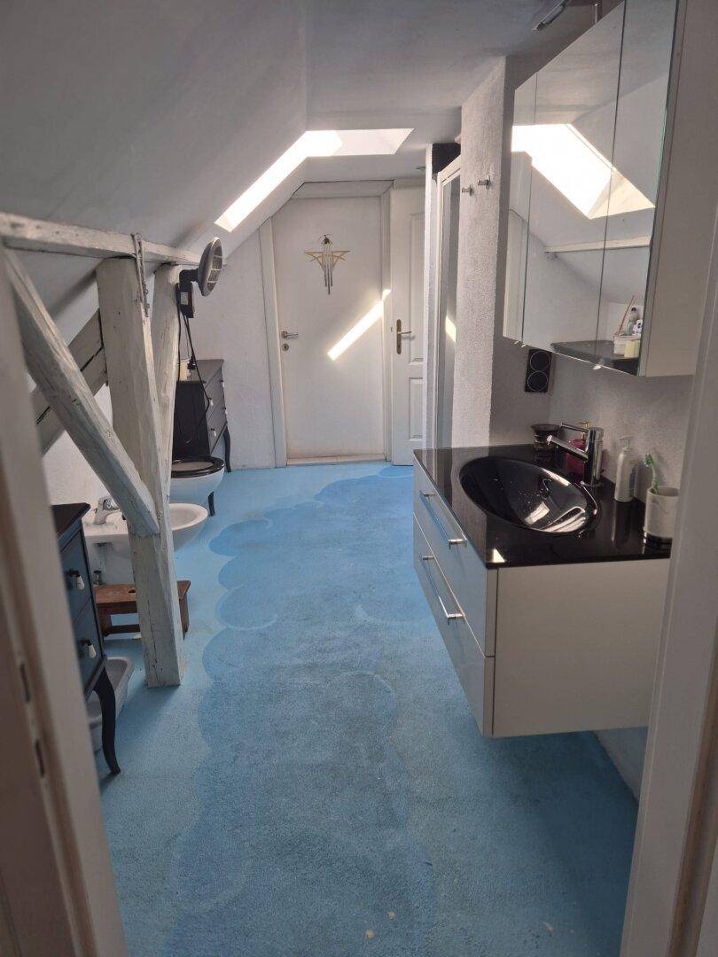 Badezimmer im Dachgeschoss mit blauer Bodenfarbe, Waschbecken, Spiegelschrank und Dachfenster.