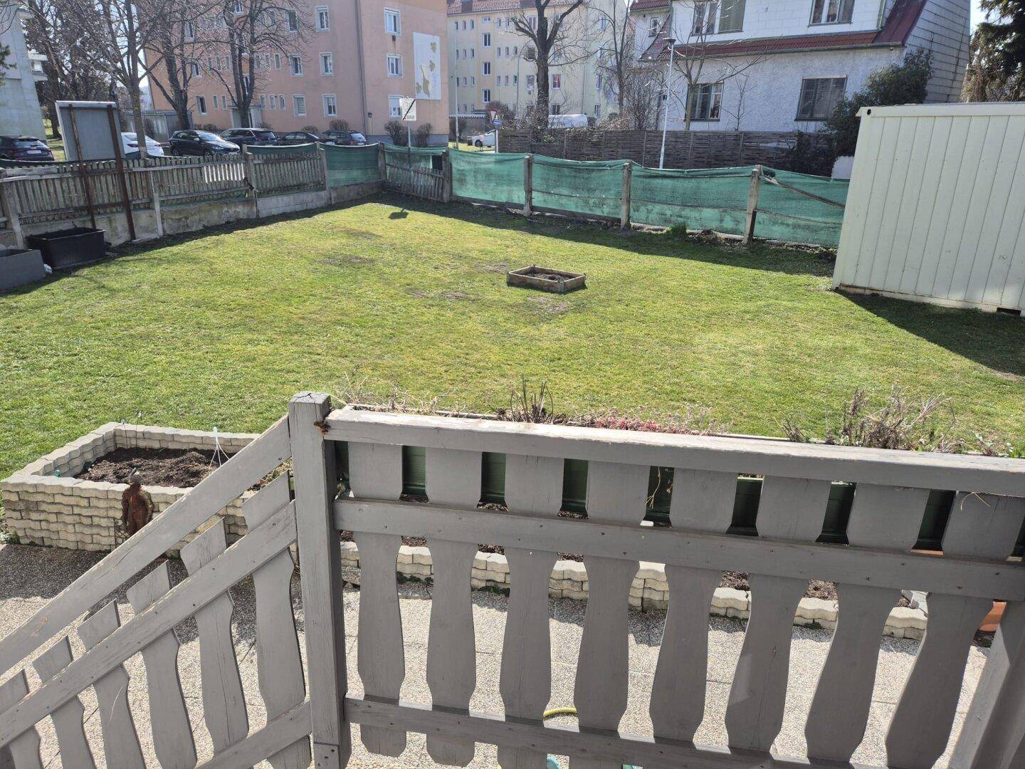 Grüner Gartenbereich mit Rasenfläche, Hochbeet und Blick auf die umliegenden Gebäude.