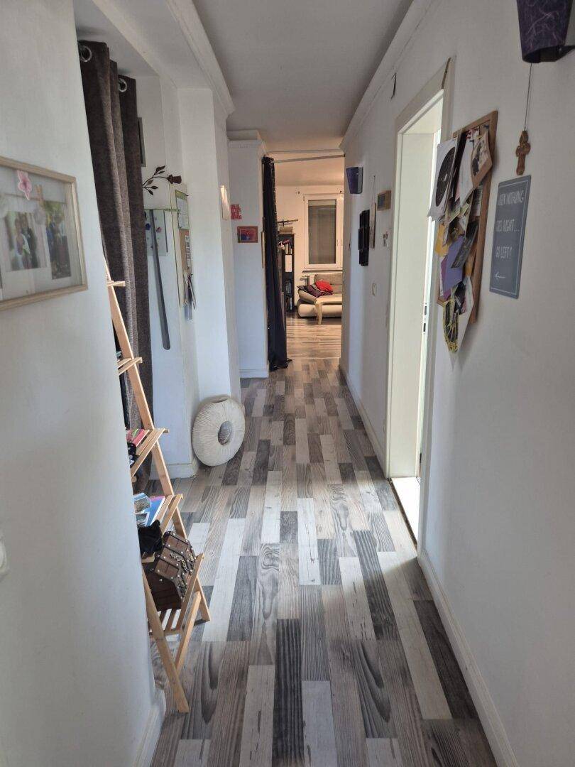 Langer Flur mit Holzoptik-Boden, weißen Wänden und Durchgang zu verschiedenen Zimmern.