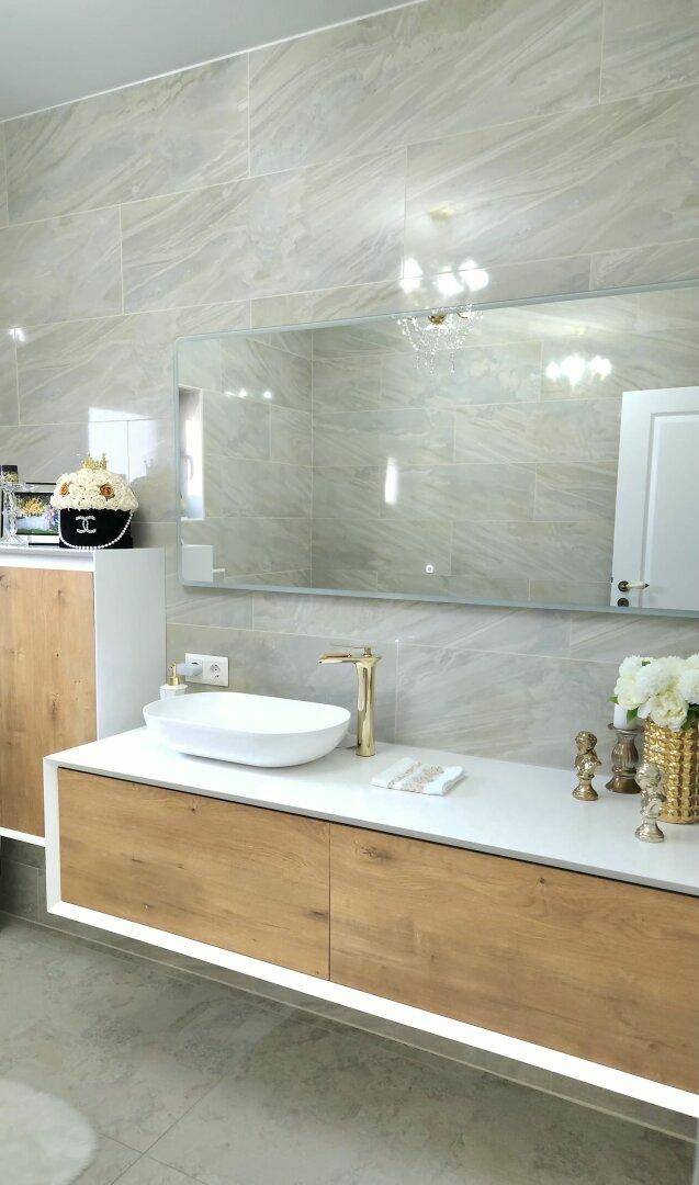 Modernes Badezimmer mit großformatigen Fliesen, schwebendem Waschtisch und goldenen Armaturen.
