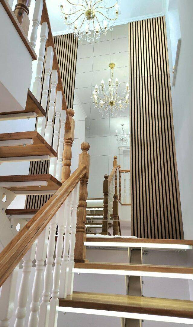 Elegantes Treppenhaus mit Holzstufen, weißen Geländern und dekorativer Wandverkleidung.