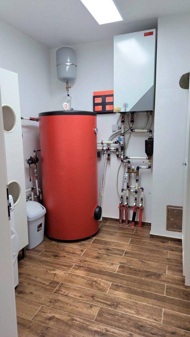 Technikraum mit Warmwasserspeicher und Heizungsanlage auf Fliesenboden.