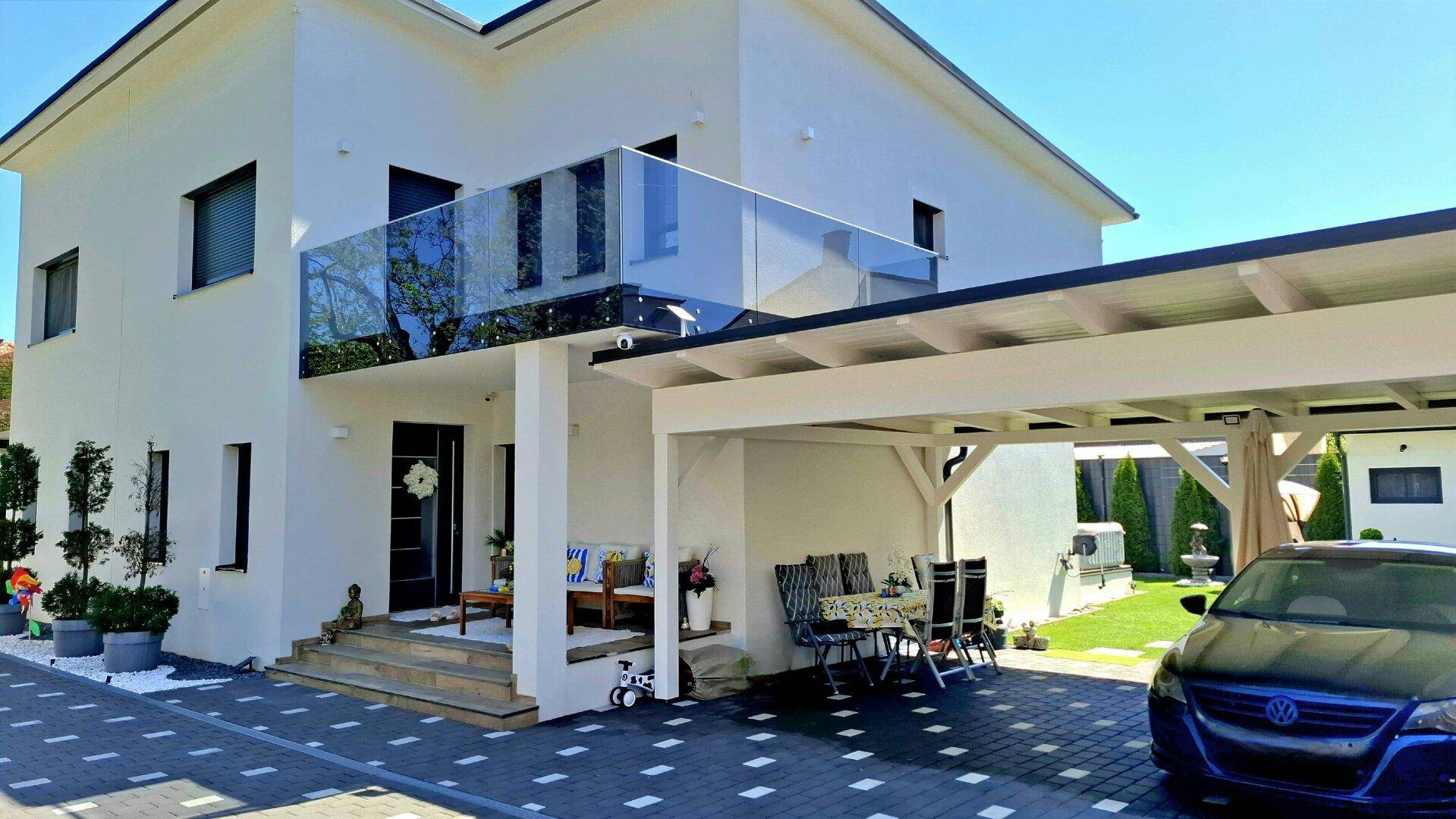 Eingangsbereich des Hauses mit überdachtem Carport, Sitzgelegenheiten und Glasbalkon.