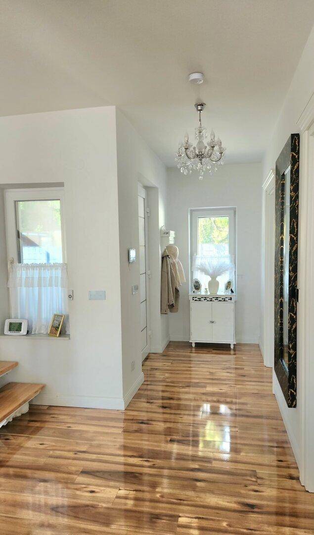 Heller Flur mit glänzendem Holzfußboden, Kronleuchter und weißer Einrichtung.