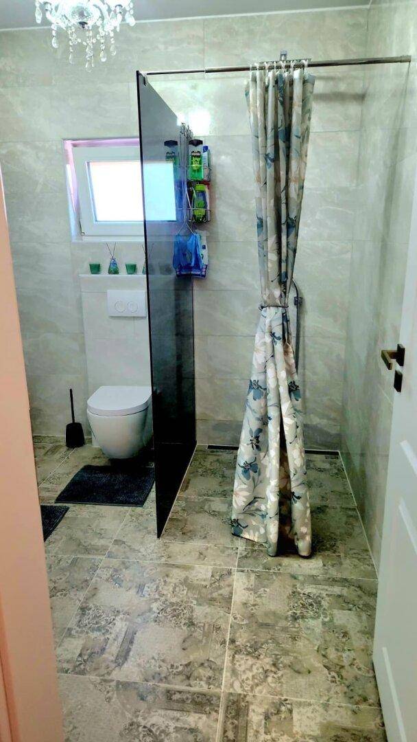 Funktionales Badezimmer mit Toilette, Duschbereich und hellen Fliesen.