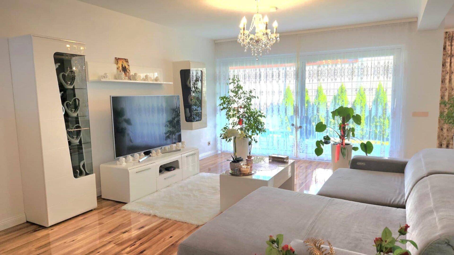 Geräumiges Wohnzimmer mit bequemer Couch, Fernseher und großen Fenstern zum Garten.