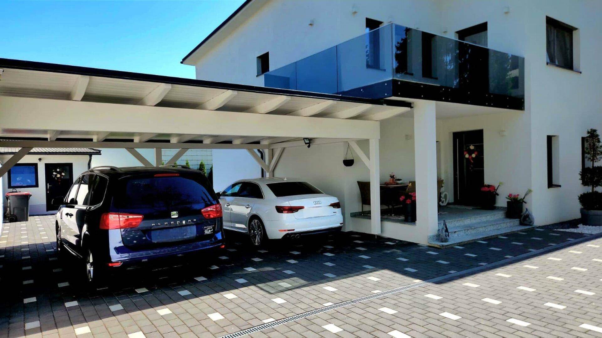 Moderne Hausfassade mit Doppelcarport und einem Balkon mit Glasgeländer.