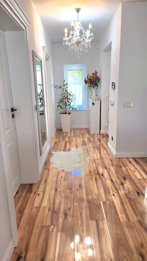 Heller Flur mit glänzendem Holzfußboden und einem eleganten Kronleuchter.