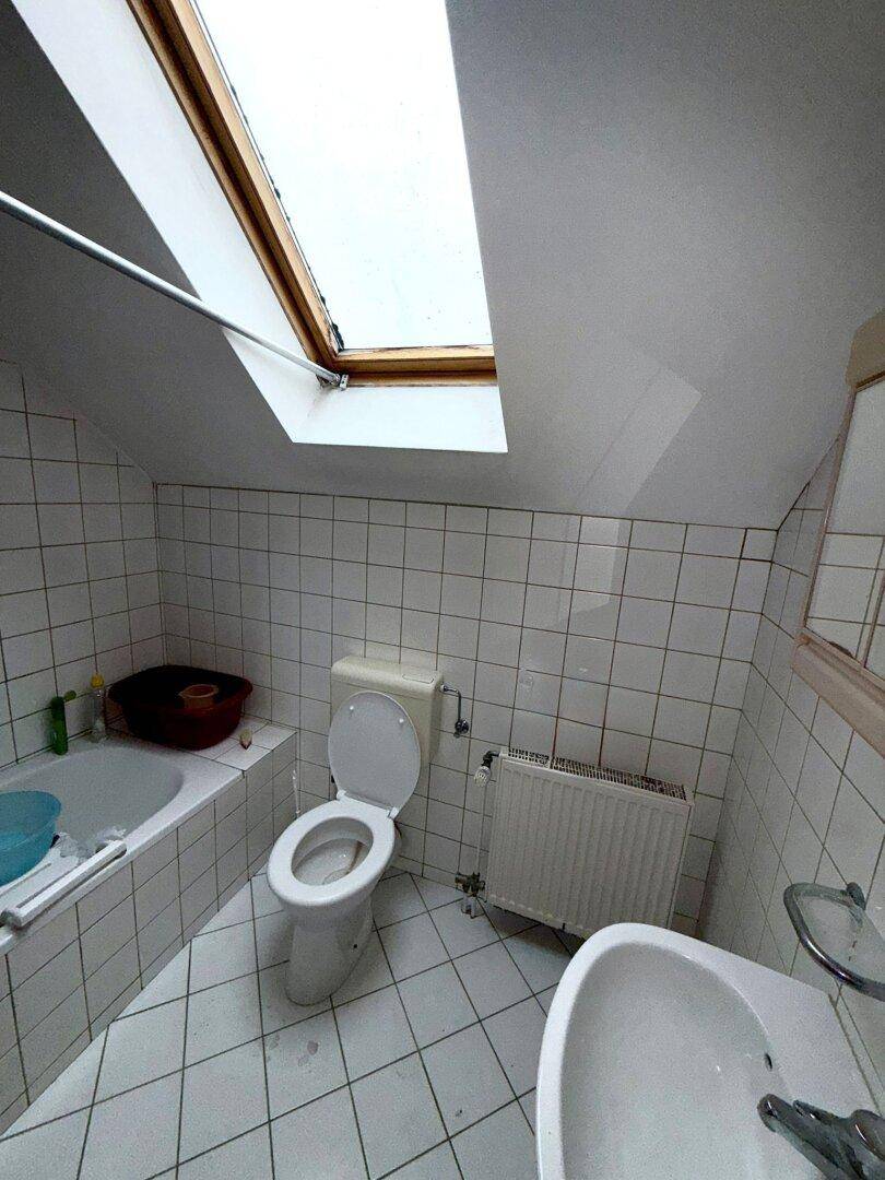 Badezimmer im Dachgeschoss mit Badewanne, WC, Waschbecken und Dachfenster, hell und funktional.