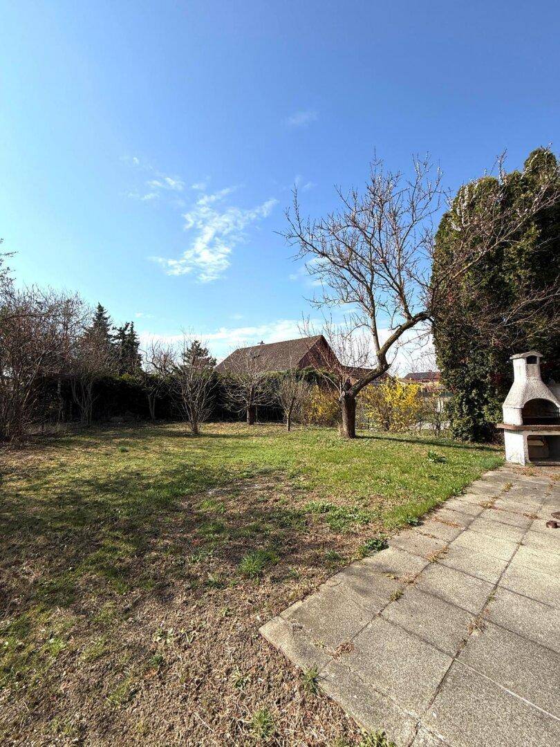 Weitläufiger Gartenbereich mit Rasen, Bäumen und gemauertem Grillplatz, ideal für Freizeit.