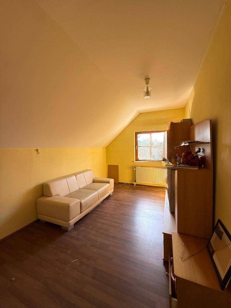 Gemütliches Schlafzimmer im Dachgeschoss mit Schrägen, Sofa und Holzboden, hell und einladend.
