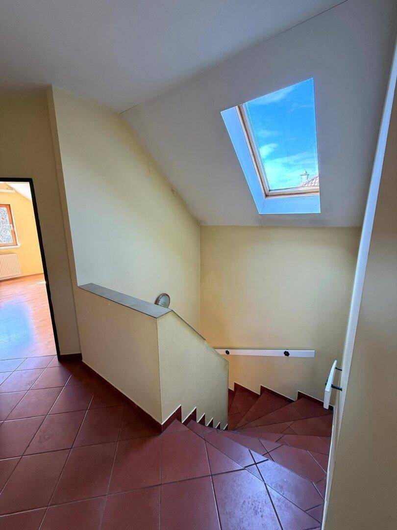 Treppenhaus mit roten Fliesen, Handlauf und Dachfenster für natürliches Licht im Obergeschoss.