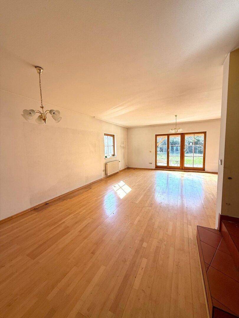Heller Wohnbereich mit Holzboden und großen Fenstern zum Garten, gut beleuchtet.