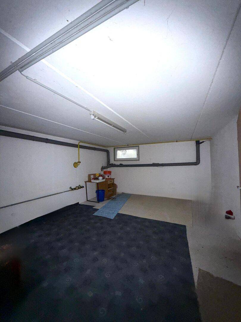 Kellerraum mit Betonboden, kleinem Fenster und sichtbaren Leitungen, ideal als Abstellraum.