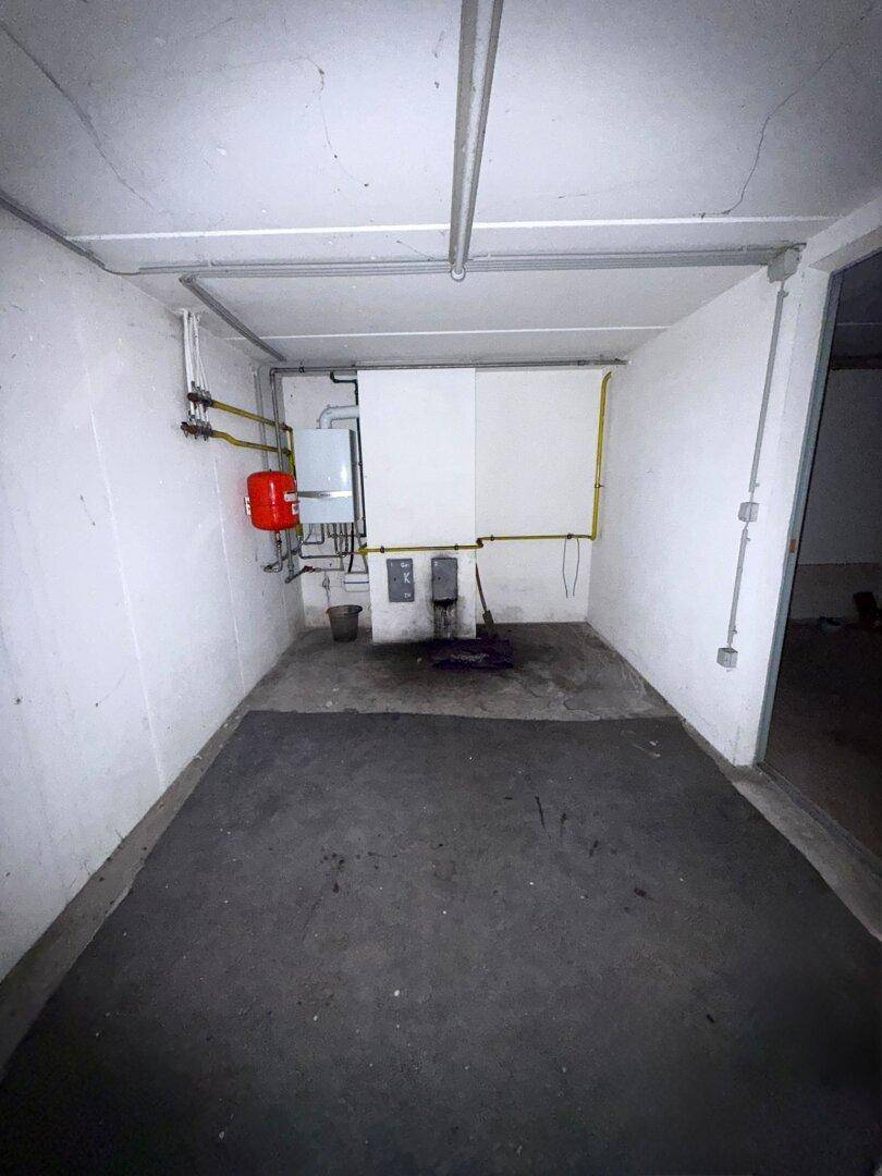 Heizungsraum im Keller mit Boiler, Leitungen und Betonboden, funktional und geräumig.