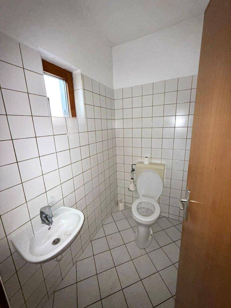 Kleines Gäste-WC mit weißen Wand- und Bodenfliesen sowie Fenster, funktional und hell.