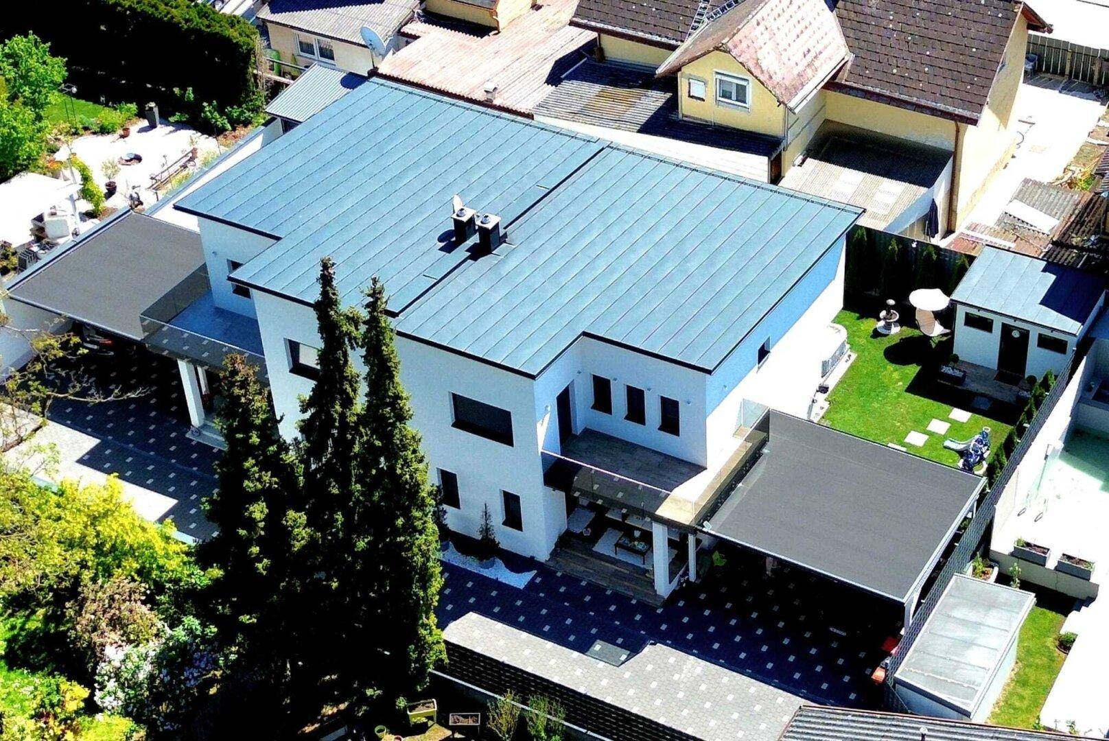 Luftaufnahme eines modernen Einfamilienhauses mit Flachdach, Carport und gepflegtem Gartenbereich.