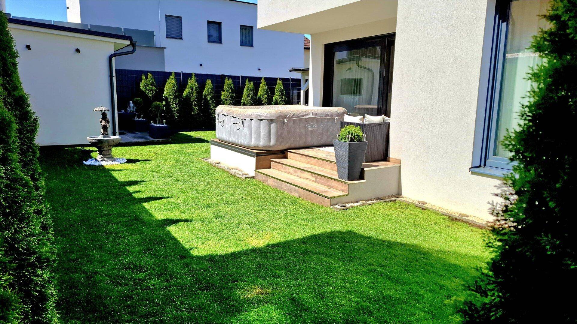 Entspannender Whirlpool im gepflegten Gartenbereich neben der modernen Hausfassade.