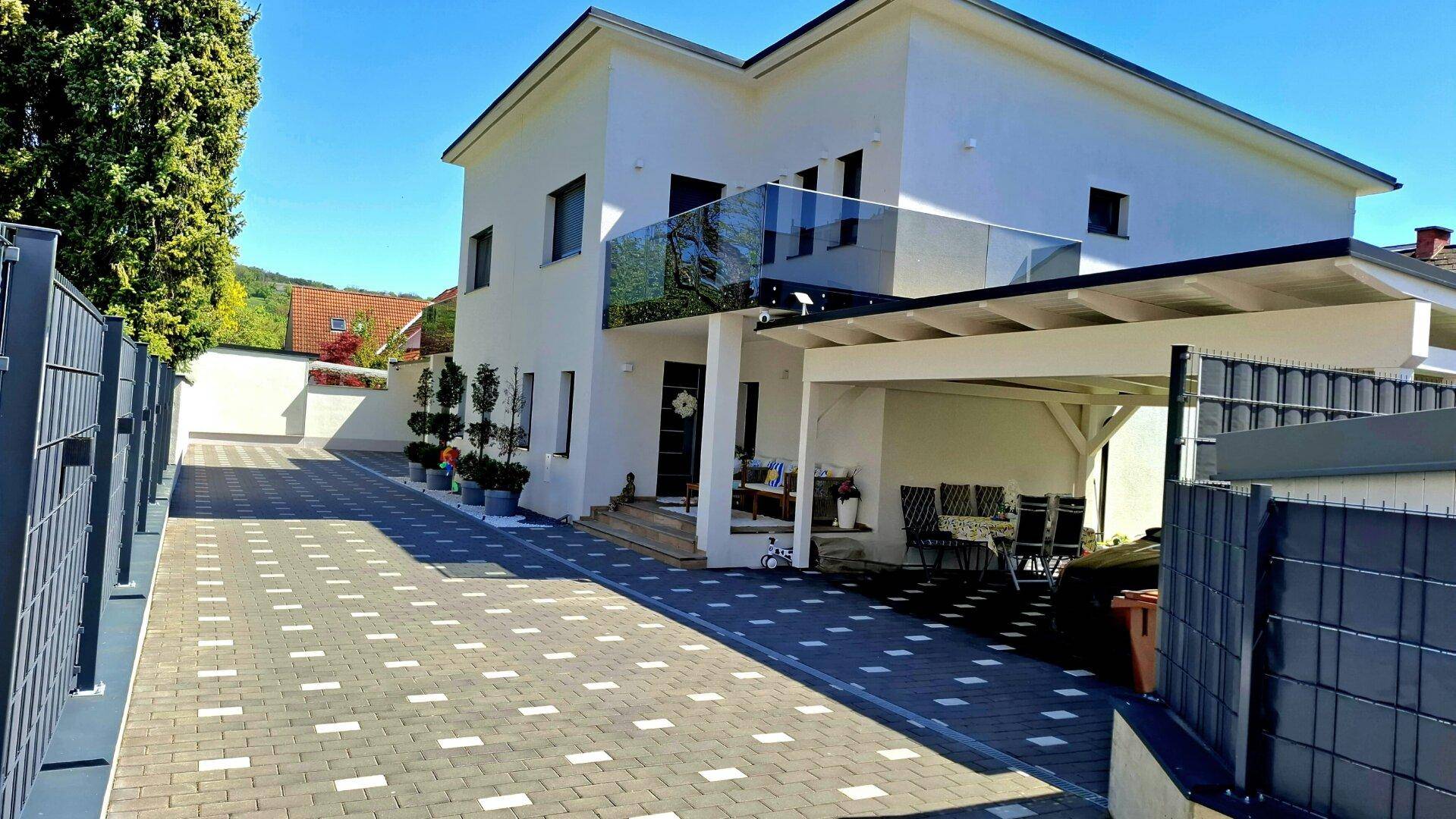 Elegante moderne Hausfassade mit großzügiger Auffahrt und einem Balkon mit Glasgeländer.