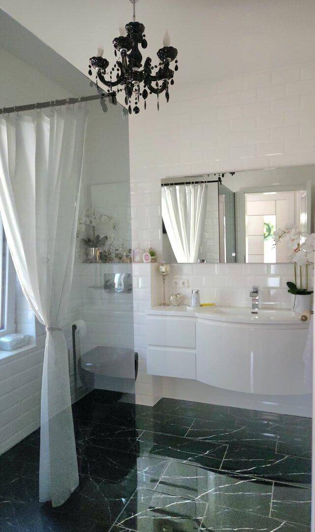 Modernes Badezimmer mit dunklen Marmorfliesen, weißem Waschtisch und stilvollem Kronleuchter.