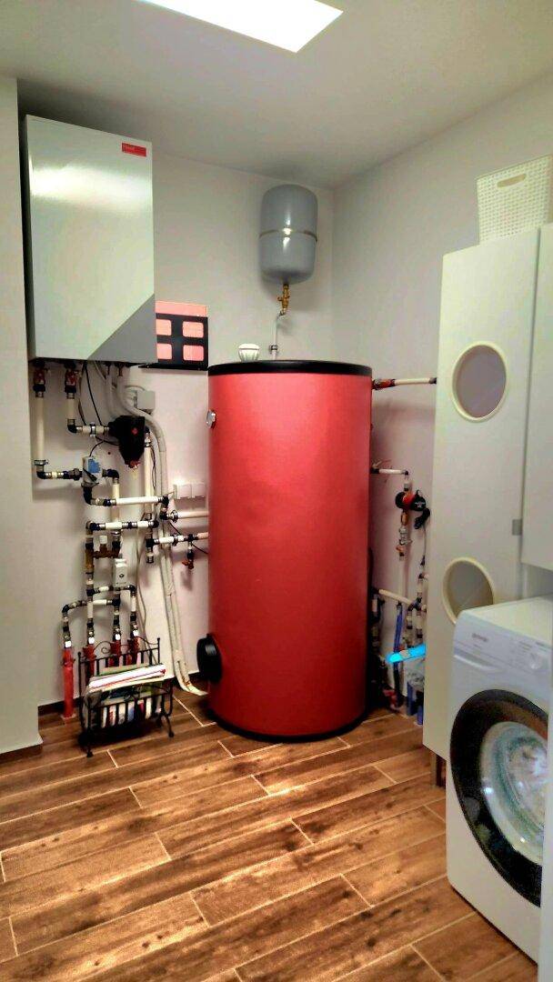 Funktionaler Hauswirtschaftsraum mit Warmwasserspeicher, Installationen und Waschmaschine.