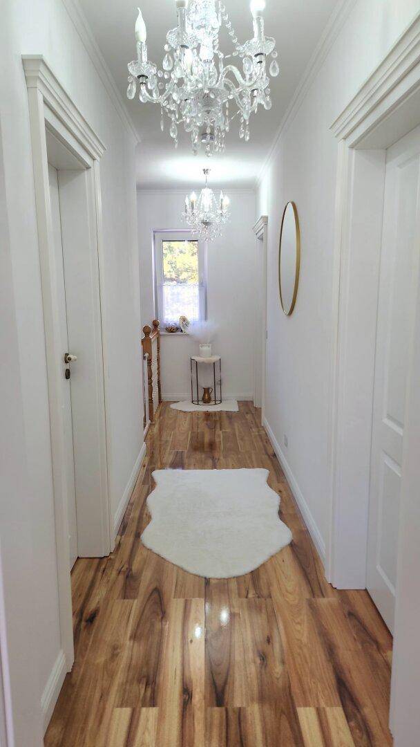Langer heller Flur im Obergeschoss mit Holzfußboden und mehreren eleganten Kronleuchtern.