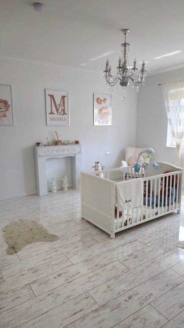Freundliches Kinderzimmer mit Babybett, dekorativem Kamin und hellem Holzboden.