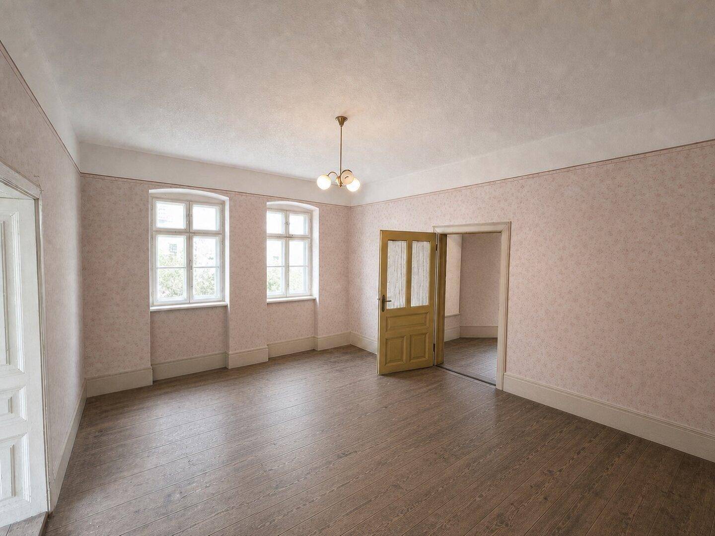 Leerer Raum mit Holzdielenboden, zwei Fenstern und einer schlichten Deckenleuchte.