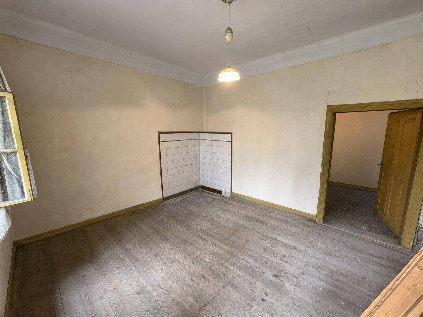 Leerer Raum mit Holzdielenboden, einem Fenster und gefliestem Eckbereich.