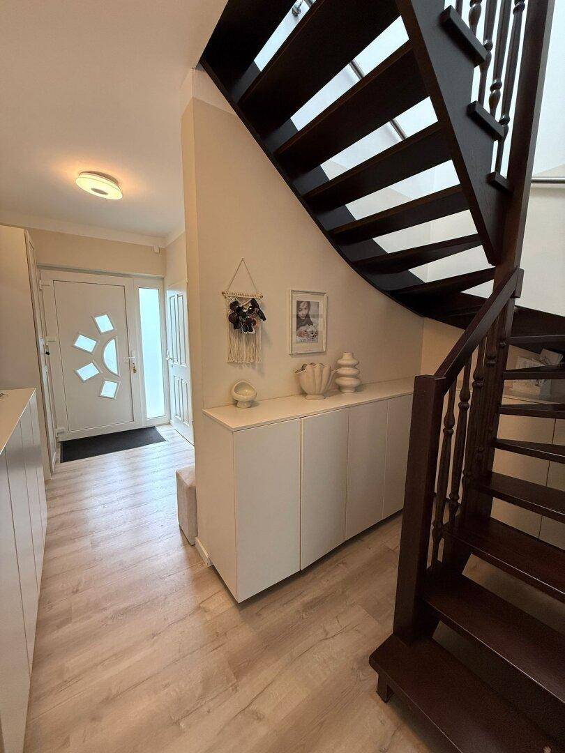 Eingangsbereich mit dunkler Holztreppe und hellem Laminatboden, modern eingerichtet.