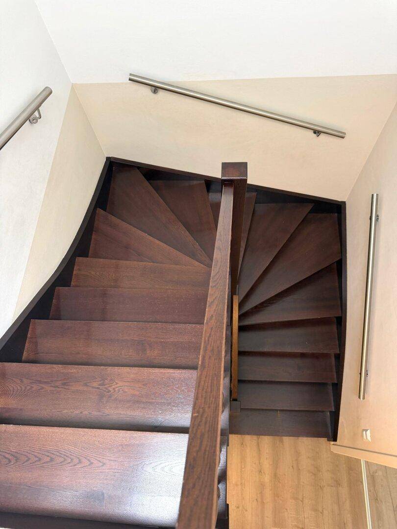 Dunkle Holztreppe mit Metallgeländer, die in die obere Etage führt.