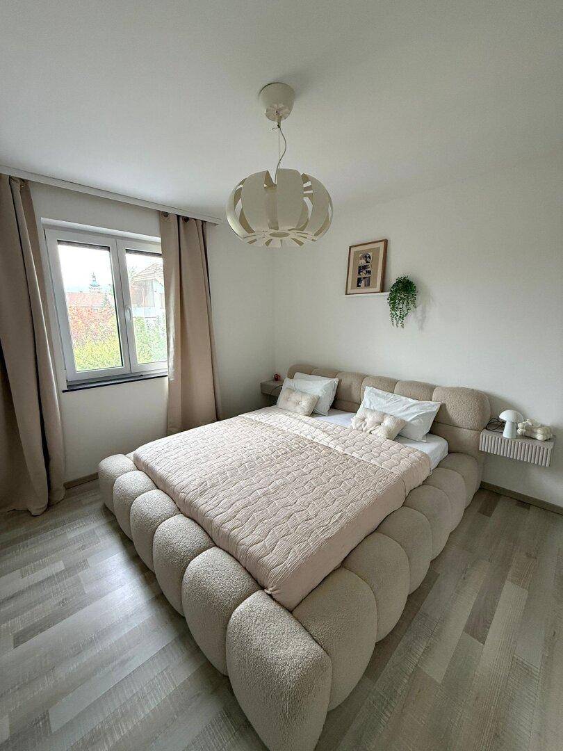 Gemütliches Schlafzimmer mit großem, gepolstertem Bett und hellem Laminatboden.