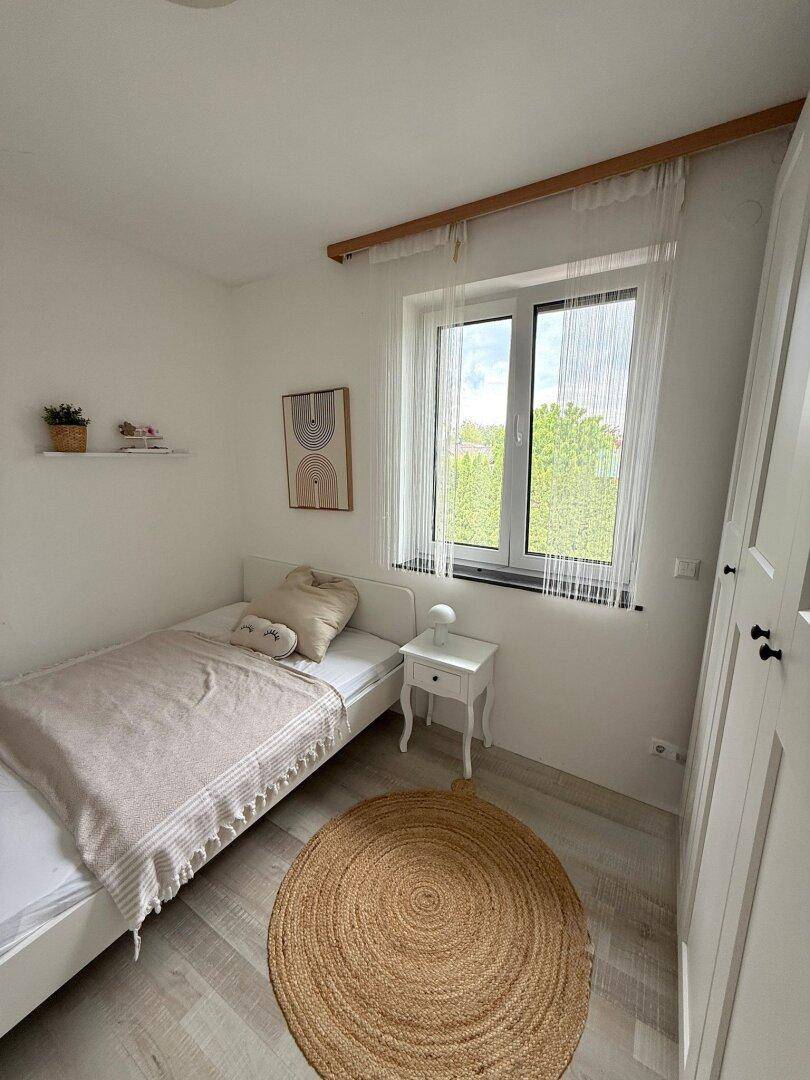 Helles Kinderzimmer mit Einzelbett, Laminatboden und Fenster mit Blick ins Grüne.
