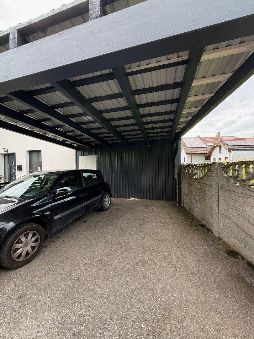 Überdachter Stellplatz für ein Auto, mit robustem Holzrahmen und Wellblechdach.