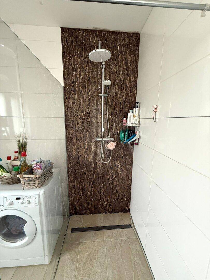 Modernes Badezimmer mit begehbarer Dusche, Waschmaschine und Fliesenboden.