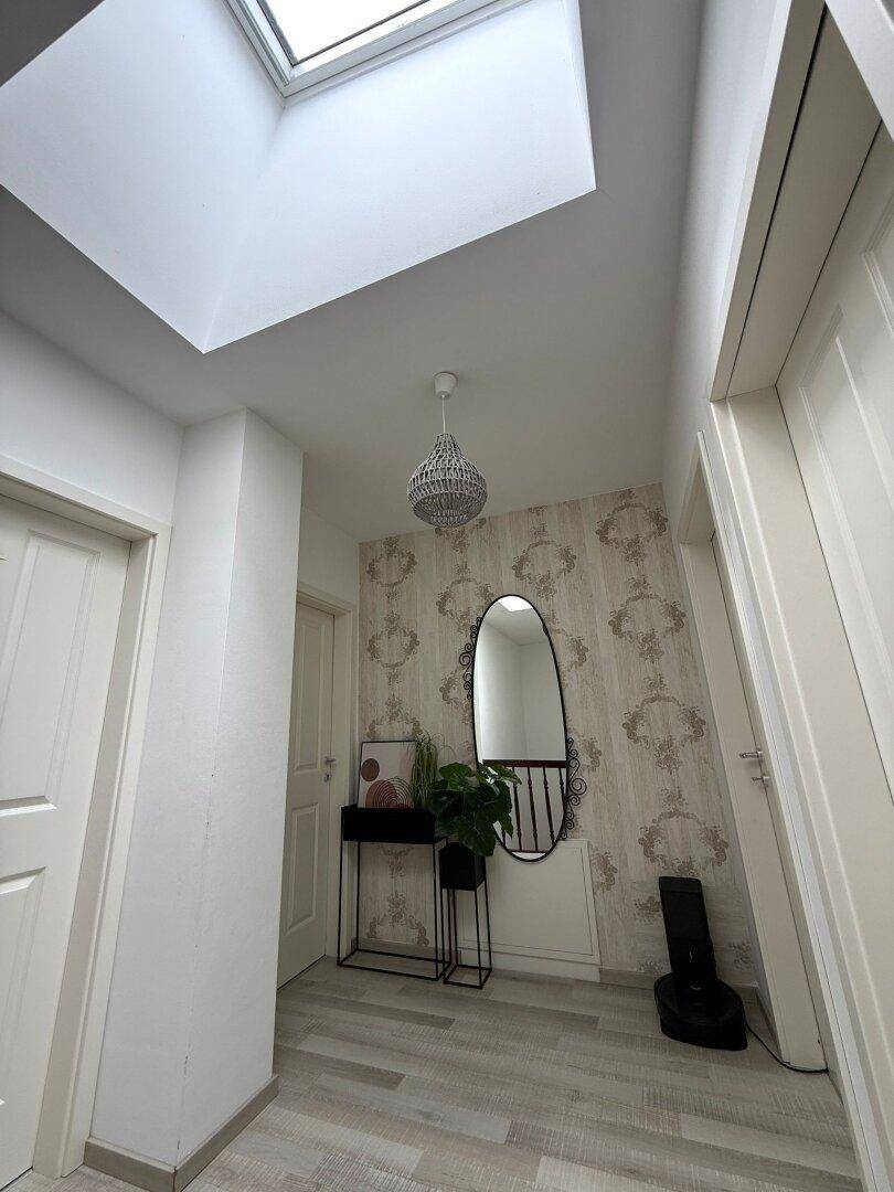 Heller Flur mit Dachfenster, gemusterter Tapete und modernem Spiegel.
