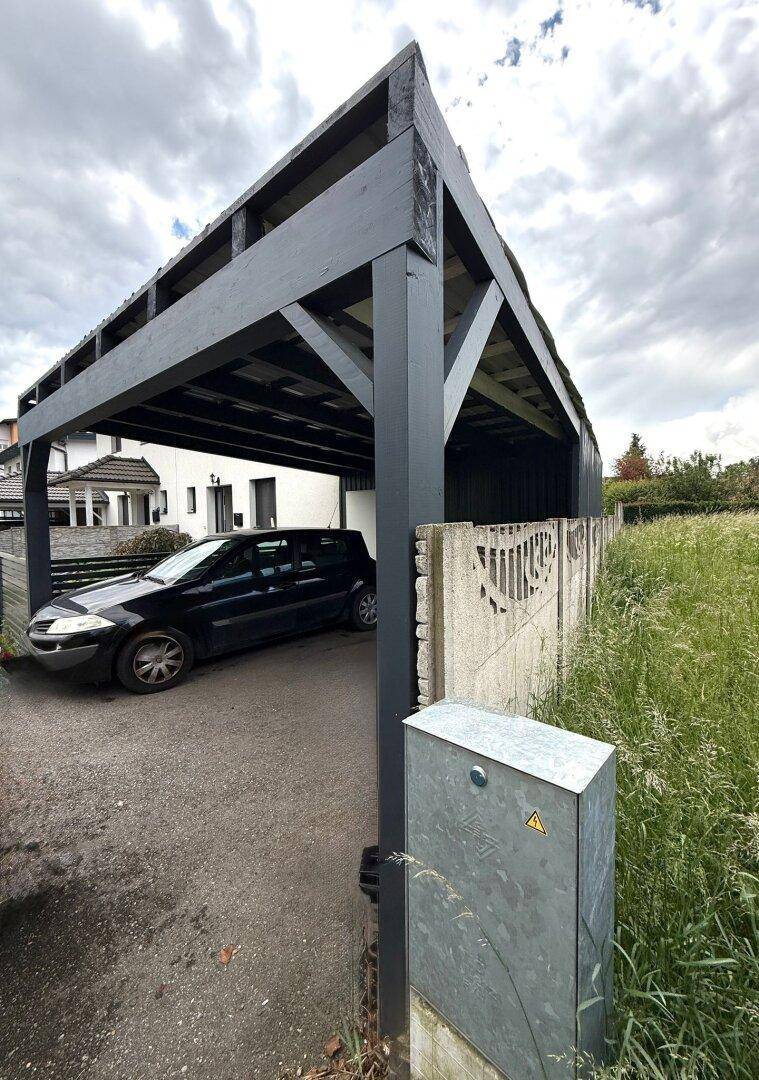 Geräumiger Carport mit Holzkonstruktion und angrenzendem Grünbereich.