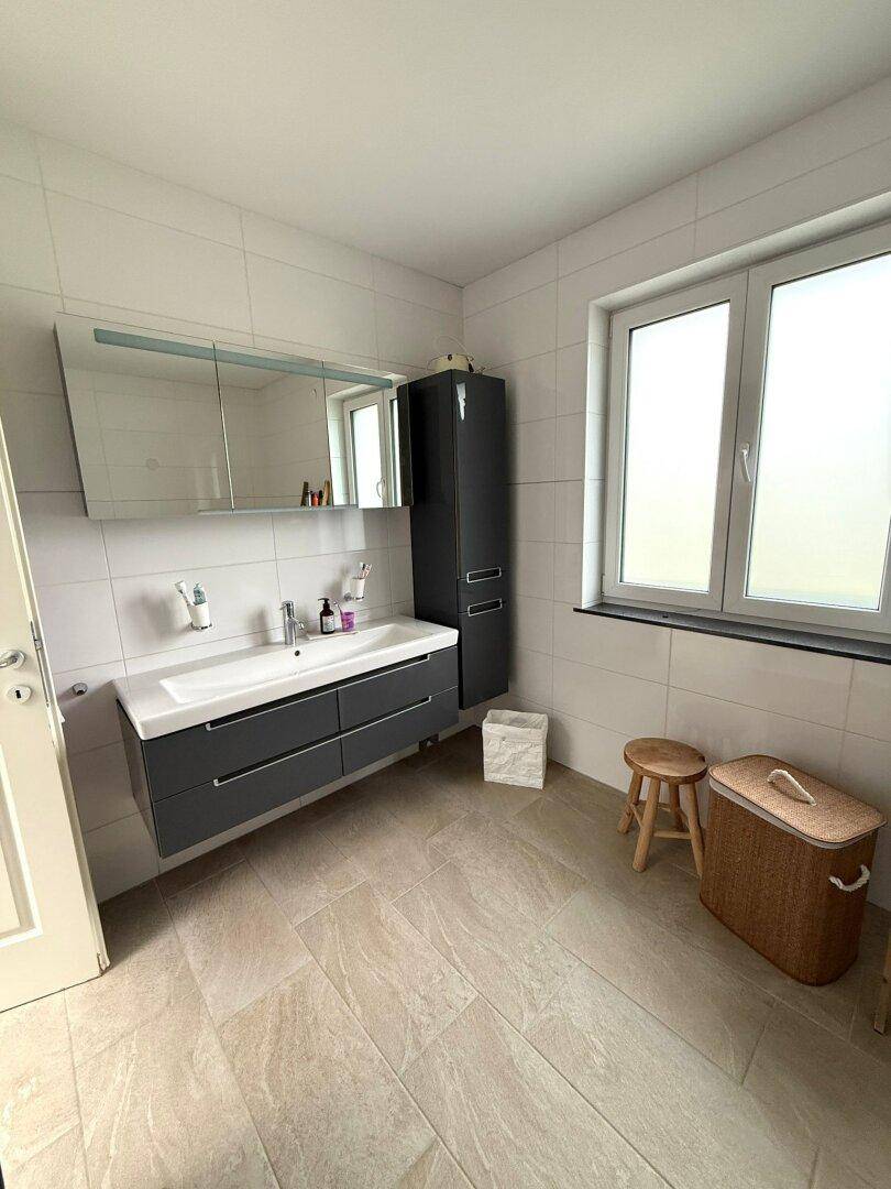 Helles Badezimmer mit modernem Waschtisch, Spiegelschrank und Fenster.