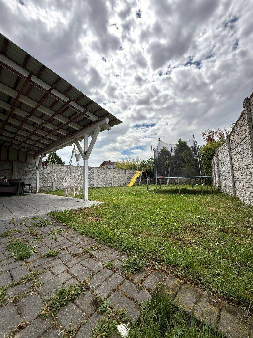 Gartenbereich mit Rasenfläche, Trampolin und überdachter Terrasse.
