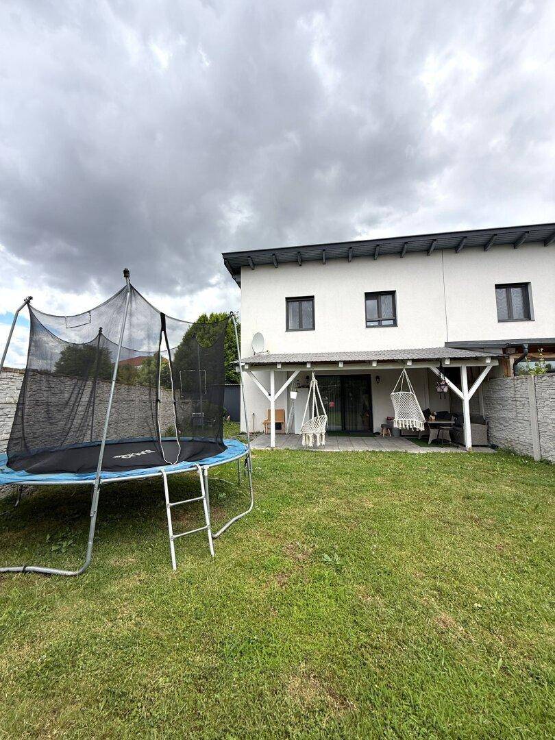 Hinterhof mit Rasen, Trampolin und überdachter Terrasse am Haus.