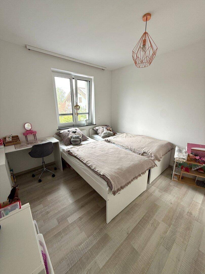 Kinderzimmer mit zwei Einzelbetten, Schreibtisch und hellem Laminatboden.