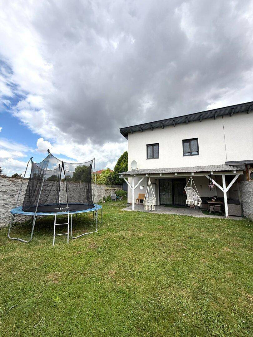 Gepflegter Garten mit Rasenfläche, Trampolin und überdachtem Sitzbereich.